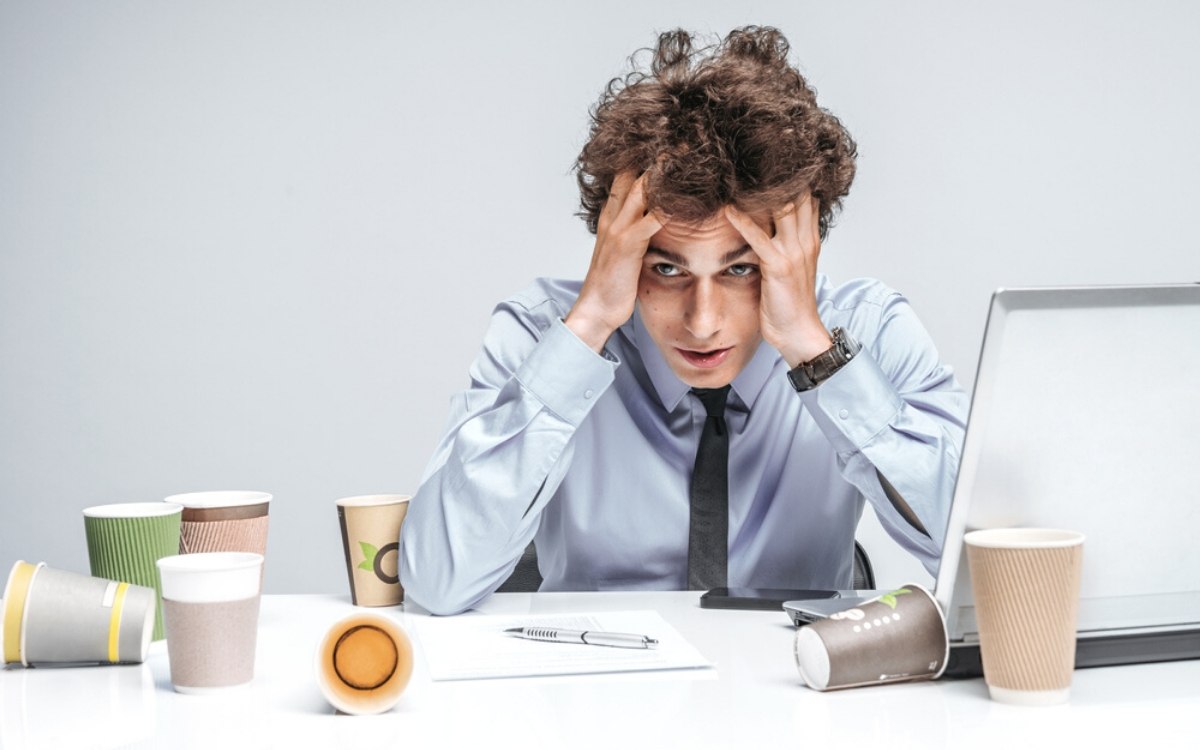 Man working harder at desk with empty coffee cups